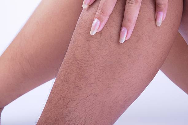 A woman's french manicured hand rests on her knee, while her lower leg shows long dark leg hair growth.
